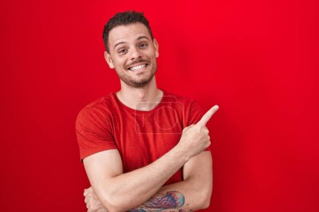 Photo for Young hispanic man standing over red background with a big smile on face, pointing with hand finger to the side looking at the camera. - Royalty Free Image