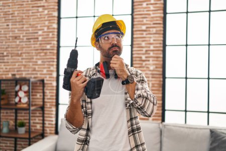 Photo for Young hispanic man with beard working at home renovation serious face thinking about question with hand on chin, thoughtful about confusing idea - Royalty Free Image