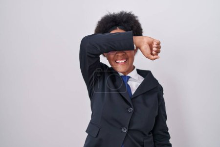 Téléchargez les photos : Belle femme africaine aux cheveux bouclés portant une veste d'affaires et des lunettes couvrant les yeux avec le bras souriant gai et drôle. concept aveugle. - en image libre de droit
