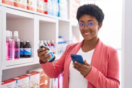 Téléchargez les photos : African american woman customer using smartphone holding medication bottle at pharmacy - en image libre de droit