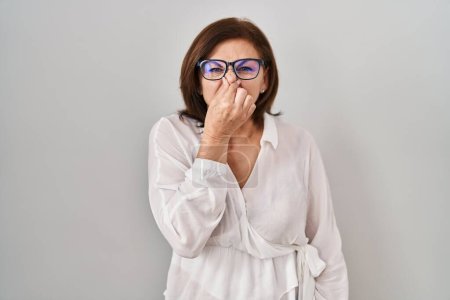 Photo for Middle age hispanic woman standing over isolated background smelling something stinky and disgusting, intolerable smell, holding breath with fingers on nose. bad smell - Royalty Free Image