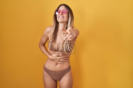 Photo for Young hispanic woman wearing bikini over yellow background laughing at you, pointing finger to the camera with hand over body, shame expression - Royalty Free Image