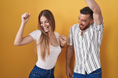 Téléchargez les photos : Jeune couple debout sur fond jaune dansant heureux et joyeux, souriant décontracté et confiant écoutant de la musique - en image libre de droit