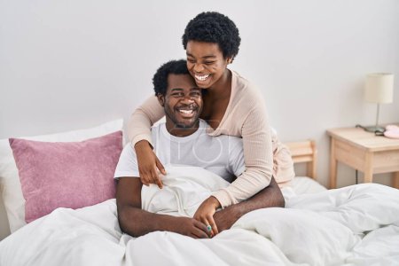 Téléchargez les photos : Africain américain homme et femme couple étreignant l'autre assis sur le lit à chambre - en image libre de droit