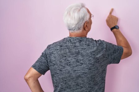 Photo for Middle age man with grey hair standing over pink background posing backwards pointing ahead with finger hand - Royalty Free Image