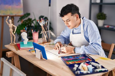 Téléchargez les photos : Jeune artiste homme non binaire utilisant le dessin tactile sur ordinateur portable au studio d'art - en image libre de droit