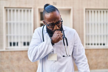 Foto de Hombre afroamericano con uniforme médico y estetoscopio sintiéndose mal y tosiendo como síntoma de resfriado o bronquitis. concepto de atención sanitaria. - Imagen libre de derechos