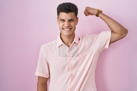 Photo for Young hispanic man standing over pink background strong person showing arm muscle, confident and proud of power - Royalty Free Image