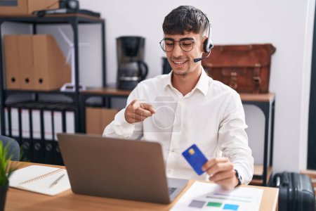 Photo for Young hispanic man working using computer laptop holding credit card pointing to you and the camera with fingers, smiling positive and cheerful - Royalty Free Image