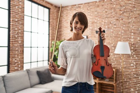 Téléchargez les photos : Young beautiful hispanic woman musician smiling confident holding violin at home - en image libre de droit