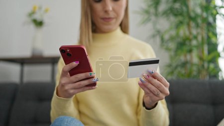 Foto de Joven rubia de compras con smartphone y tarjeta de crédito en casa - Imagen libre de derechos