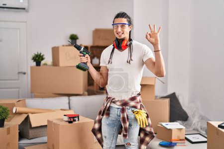 Photo for Hispanic man with long hair holding screwdriver at new home doing ok sign with fingers, smiling friendly gesturing excellent symbol - Royalty Free Image
