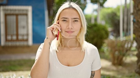Foto de Joven hermosa mujer hispana sonriendo confiada hablando en el teléfono inteligente en el parque - Imagen libre de derechos