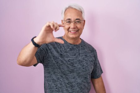 Photo for Middle age man with grey hair standing over pink background smiling and confident gesturing with hand doing small size sign with fingers looking and the camera. measure concept. - Royalty Free Image