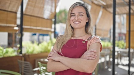 Photo for Young blonde woman waitress smiling confident standing with arms crossed gesture at coffee shop terrace - Royalty Free Image