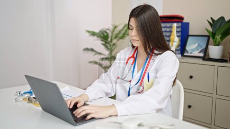 Foto de Joven hermosa mujer hispana médico utilizando portátil de trabajo en la clínica - Imagen libre de derechos