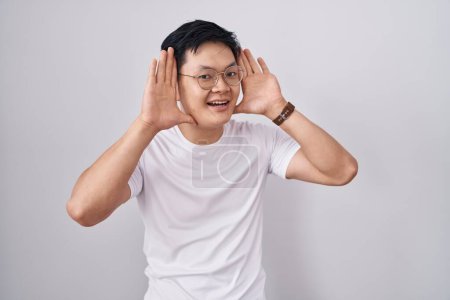 Téléchargez les photos : Jeune homme asiatique debout sur fond blanc souriant gai jouer jeter un coup d'oeil un boo avec les mains montrant le visage. surpris et sortis - en image libre de droit