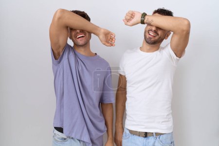 Téléchargez les photos : Couple homosexuel gay debout sur fond blanc couvrant les yeux avec le bras souriant gai et drôle. concept aveugle. - en image libre de droit