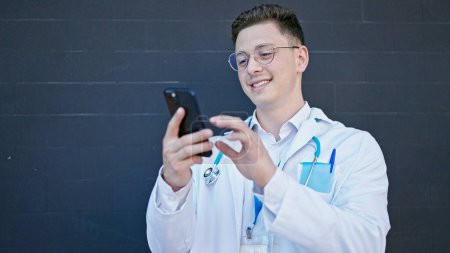 Photo for Young hispanic man doctor smiling confident using smartphone over isolated black background - Royalty Free Image