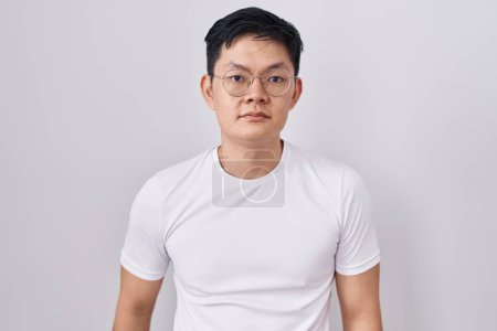 Photo for Young asian man standing over white background relaxed with serious expression on face. simple and natural looking at the camera. - Royalty Free Image