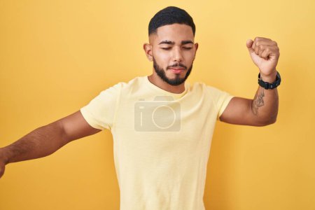 Photo for Young hispanic man standing over yellow background dancing happy and cheerful, smiling moving casual and confident listening to music - Royalty Free Image