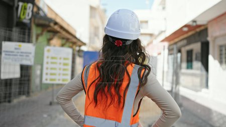 Photo for Young beautiful hispanic woman builder wearing hardhat backwards at street - Royalty Free Image