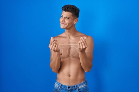 Téléchargez les photos : Jeune homme hispanique debout torse nu sur fond bleu faisant geste d'argent avec les mains, demandant le paiement du salaire, entreprise millionnaire - en image libre de droit