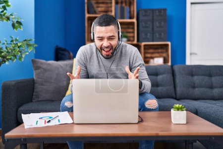 Photo for Hispanic man using laptop working from home celebrating victory with happy smile and winner expression with raised hands - Royalty Free Image