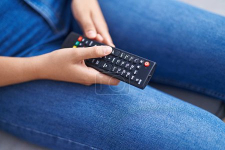 Foto de Joven hermosa mujer hispana usando control remoto de televisión sentado en el sofá en casa - Imagen libre de derechos