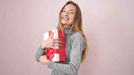 Téléchargez les photos : Jeune femme caucasienne souriante confiante tenant cadeau d'anniversaire sur fond rose isolé - en image libre de droit