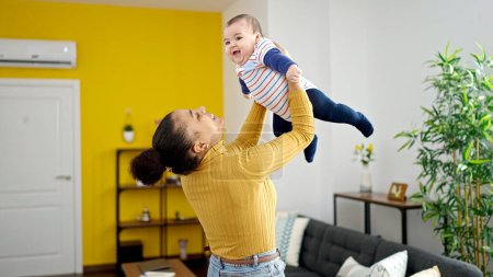 Foto de Madre e hijo sonriendo confiados sosteniendo al bebé en el aire en casa - Imagen libre de derechos