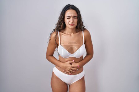 Téléchargez les photos : Jeune femme hispanique portant de la lingerie blanche avec la main sur le ventre parce que l'indigestion, la maladie douloureuse se sent mal. concept de douleur. - en image libre de droit