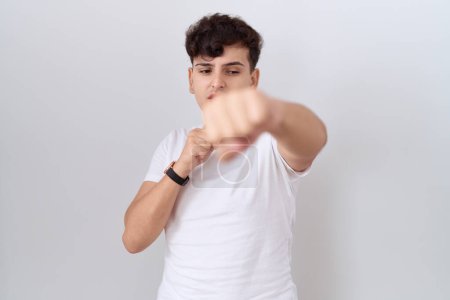 Téléchargez les photos : Jeune homme non binaire portant un t-shirt blanc décontracté poing pour se battre, agressif et en colère attaque, menace et violence - en image libre de droit