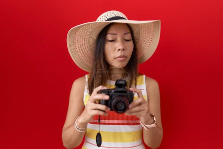 Foto de Mujer china de mediana edad usando cámara réflex con sombrero de verano expresión despistado y confuso. concepto de duda. - Imagen libre de derechos