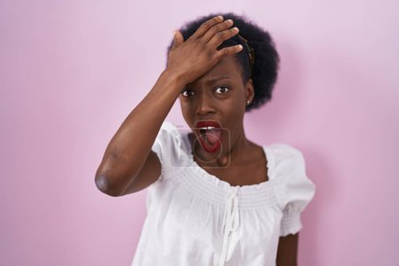 Téléchargez les photos : Femme africaine avec les cheveux bouclés debout sur fond rose surpris avec la main sur la tête pour erreur, rappelez-vous erreur. oublié, mauvais concept de mémoire. - en image libre de droit