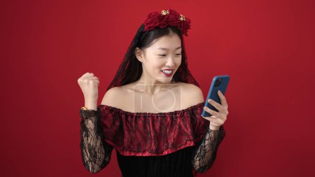 Photo for Young chinese woman wearing katrina costume using smartphone over isolated red background - Royalty Free Image