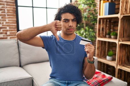 Photo for Hispanic man with curly hair holding credit card with angry face, negative sign showing dislike with thumbs down, rejection concept - Royalty Free Image