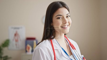 Téléchargez les photos : Jeune belle femme hispanique médecin souriant confiance debout à la clinique - en image libre de droit
