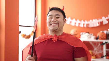 Photo for Young chinese man wearing devil costume holding trident at home - Royalty Free Image