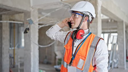 Photo for Young caucasian man architect talking on smartphone at construction site - Royalty Free Image