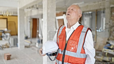 Foto de Senior hombre de pelo gris arquitecto hizo hincapié en la celebración de hardhat en el sitio de construcción - Imagen libre de derechos
