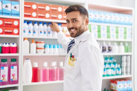 Téléchargez les photos : Jeune homme hispanique pharmacien souriant confiance debout à la pharmacie - en image libre de droit