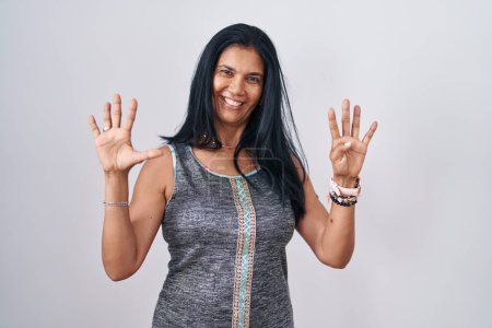 Téléchargez les photos : Femme hispanique mature debout sur fond blanc montrant et pointant vers le haut avec les doigts numéro neuf tout en souriant confiant et heureux. - en image libre de droit