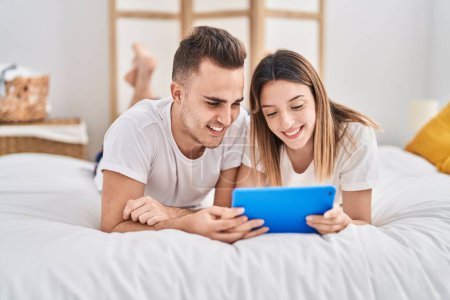 Téléchargez les photos : Homme et femme couple regarder vidéo sur touchpad couché sur lit à chambre - en image libre de droit