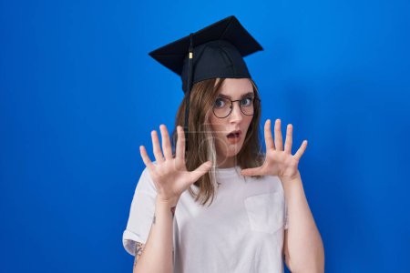 Photo for Blonde caucasian woman wearing graduation cap afraid and terrified with fear expression stop gesture with hands, shouting in shock. panic concept. - Royalty Free Image