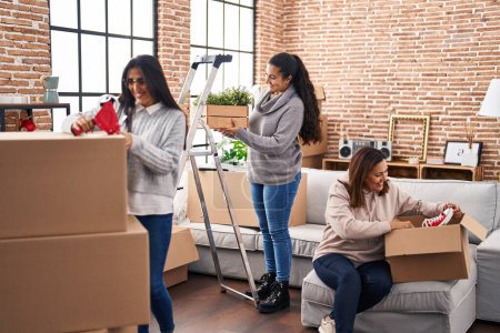 Photo for Three woman smiling confident packing cardboard box at new home - Royalty Free Image