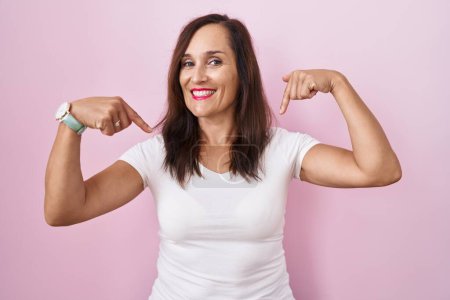 Photo for Middle age brunette woman standing over pink background looking confident with smile on face, pointing oneself with fingers proud and happy. - Royalty Free Image