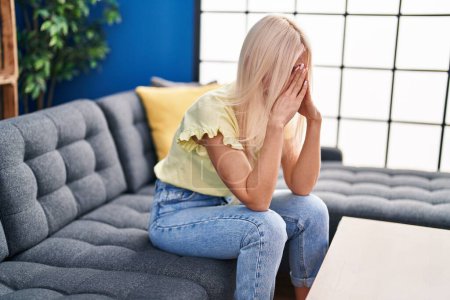 Téléchargez les photos : Jeune femme blonde déprimée assise sur un canapé à la maison - en image libre de droit