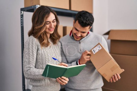 Man and woman ecommerce business workers writing on book holding package at office