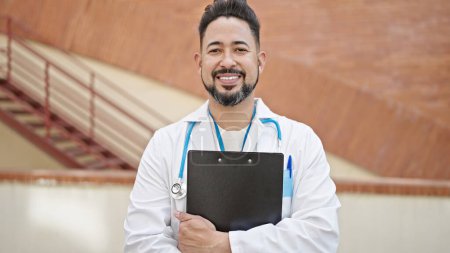 Photo for Young latin man doctor smiling confident holding medical report at hospital - Royalty Free Image